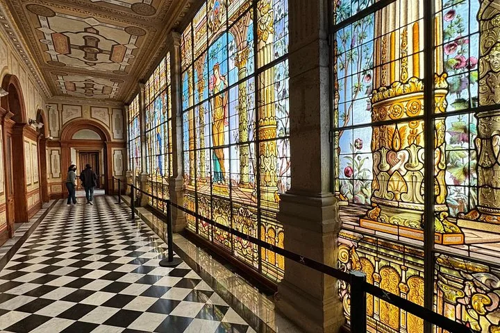 A long corridor featuring beautiful stained glass windows and a checkered floor.
