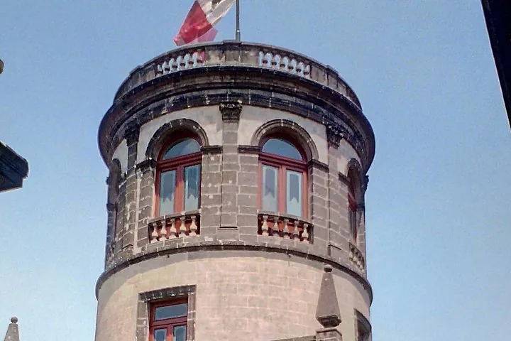 Ein Steinturm mit Bogenfenstern und einer Fahne auf der Spitze.